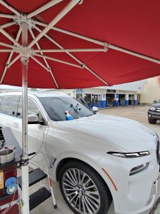 White BMW SUV getting windshield rock chip repair under red umbrella at Clint's Glass Houston